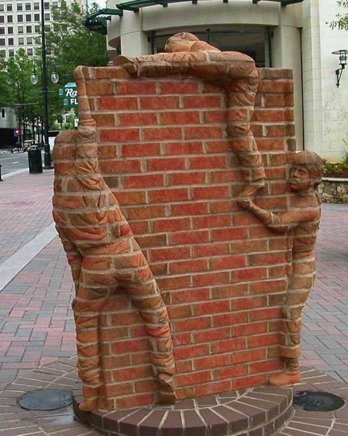 Brick sculpture by Brad Spencer in Charlotte, US, showing three children climbing a red brick wall. Their bodies are sculpted directly from the brick structure itself.
