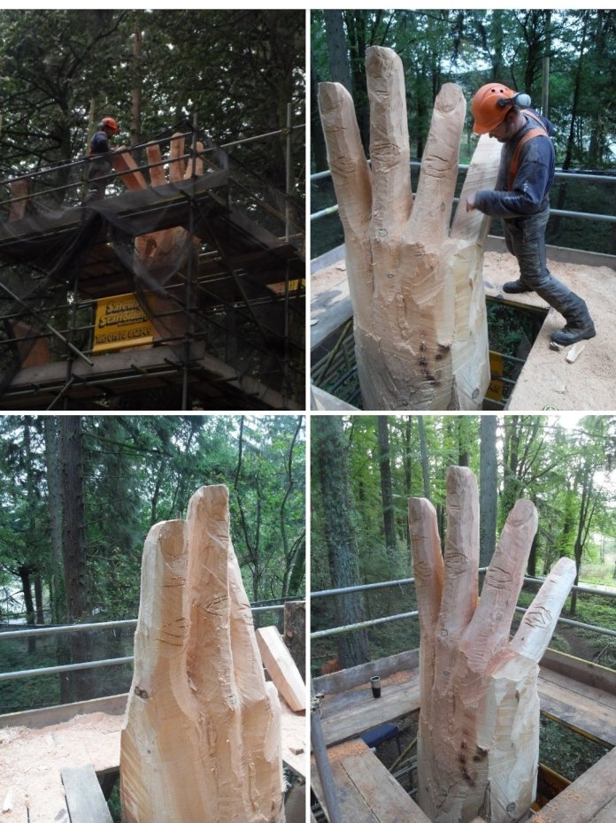 Artist Simon O’Rourke using a chainsaw to carve details into the wooden hand, with wood shavings on the ground and the partially completed sculpture visible.
