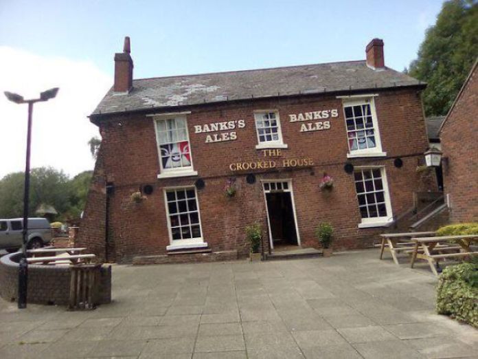 Tilted red-brick pub with angled windows and a sloping roof, the building visibly leaning to one side due to ground subsidence.