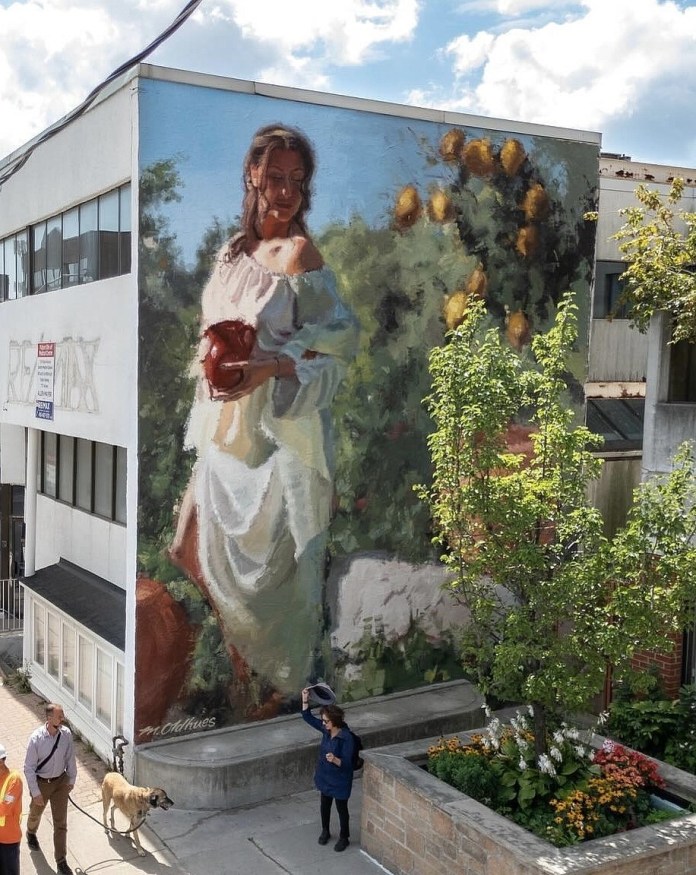 Mural on a corner building depicting a woman in a white dress holding a red jug, surrounded by green foliage and yellow flowers, painted in a textured, impressionist style.