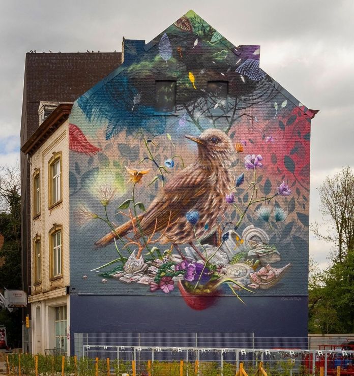 Large mural on a gabled building of a detailed brown bird surrounded by purple flowers, leaves, and smaller birds, against a background of abstract foliage patterns.