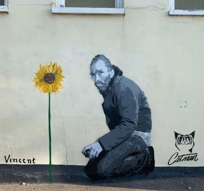 A street art mural depicting Vincent Van Gogh kneeling, holding a spray can, as if he has just painted a tall sunflower in his signature style. The mural, titled 'Vincent,' is created by artist Catman and is located in Whitstable, England. The artwork features Van Gogh in modern attire with a contemplative expression, blending historical homage with contemporary urban art.