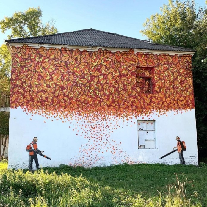 A creative street mural by Мишкин (Mishkin) in Vladimir, Russia, for 33zagfest. The artwork depicts two workers with leaf blowers seemingly dispersing a vibrant cascade of autumn leaves painted across the upper portion of a white building. The rich red, orange, and yellow hues create a dynamic scene, symbolizing the transition of seasons while honoring street art's creativity.