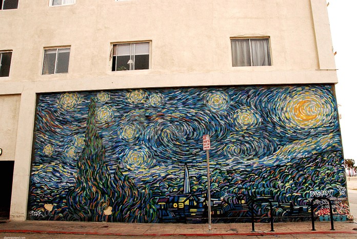 A large mural inspired by Vincent Van Gogh's Starry Night painted on the side of a beige building. The artwork vividly captures the swirling skies, glowing stars, and towering cypress tree of Van Gogh's iconic painting, reimagined in a modern urban setting. Graffiti tags at the bottom add a contemporary layer to the classical homage, blending fine art with street culture.