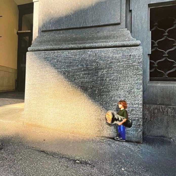Street Art of a boy holding a flashlight, with a real shaft of sunlight falling in line with the beam, creating an interactive lighting effect.