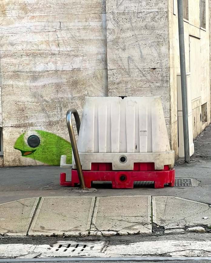 Painted turtle head and legs emerging from behind a red-and-white plastic tank, which looks like the turtle’s shell from the street.