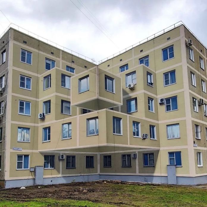 3D street art mural by Shozy in Solnechnogorsk, Russia, showing a cube-like illusion of protruding balconies on the facade of a beige apartment block, using trompe-l’oeil techniques.