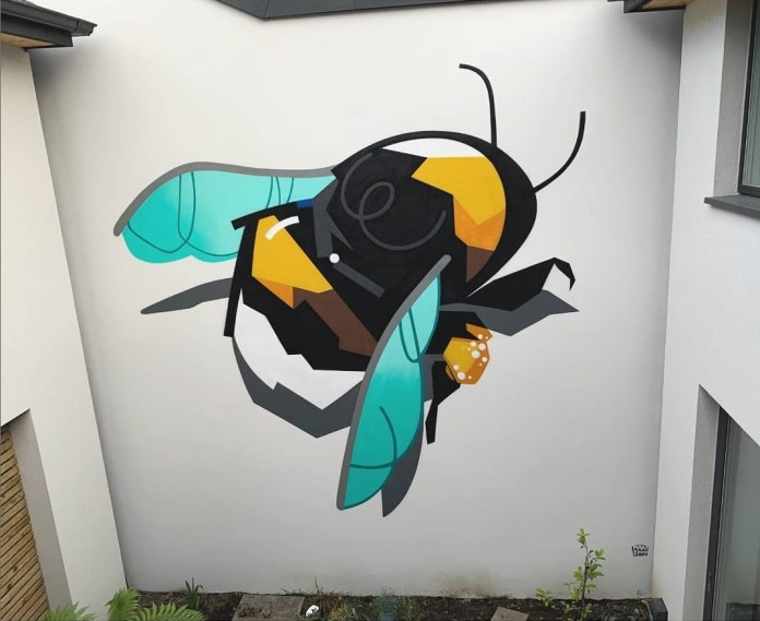 Geometric mural of a stylized bee with turquoise wings and angular yellow and black body painted on a modern white building wall.
