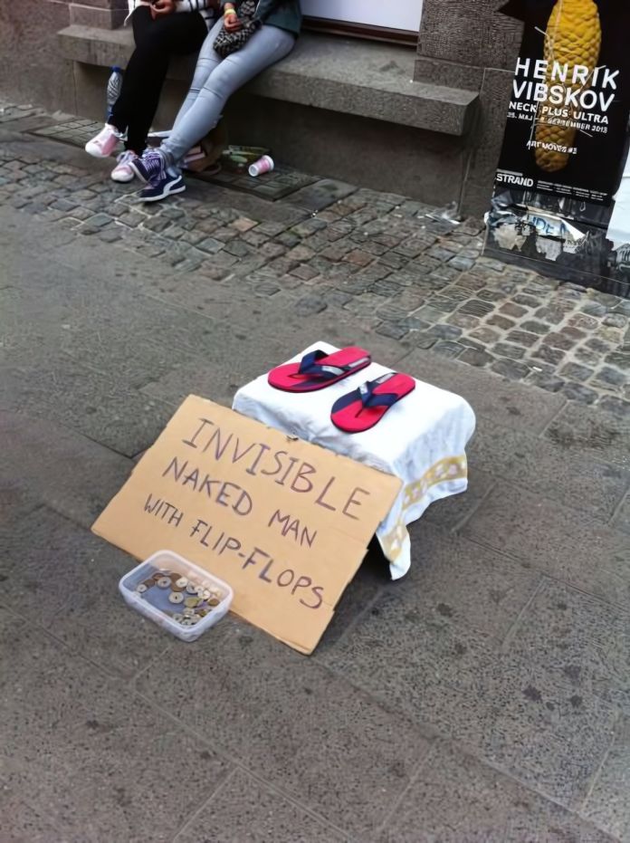 A pair of flip-flops placed on a small stool with a white cloth and a sign reading "INVISIBLE NAKED MAN WITH FLIP-FLOPS" beside a transparent container for donations, set on a cobblestone street.