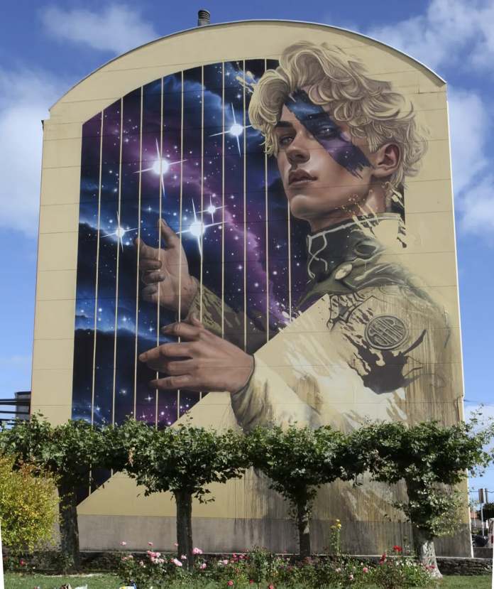 "Anf10n" by SFHIR in Fene, Spain, created for Perla Mural Fest. The mural depicts a modern interpretation of the Greek mythological figure Amphion, blending cosmic elements with human inspiration. A young man with a starry gaze and a harp-like wall symbolizes music as a force that connects rather than divides, inspired by the muses of inner creativity.
