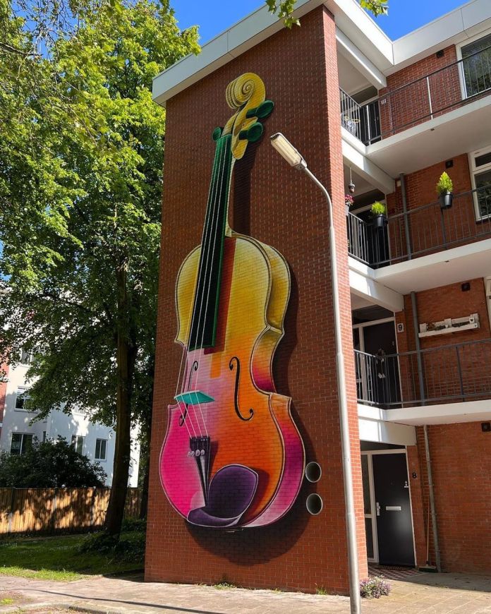Brightly colored violin mural painted vertically on the side of a brick apartment building, integrating perfectly with the architecture.