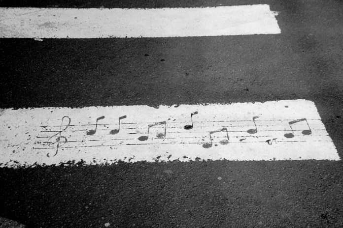 Pedestrian crosswalk painted with musical notes on the white stripes, humorously turning the road into a musical score.