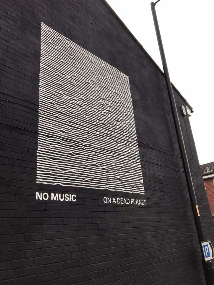 Minimalist mural of white waveforms on a black background with the text: "No music on a dead planet."