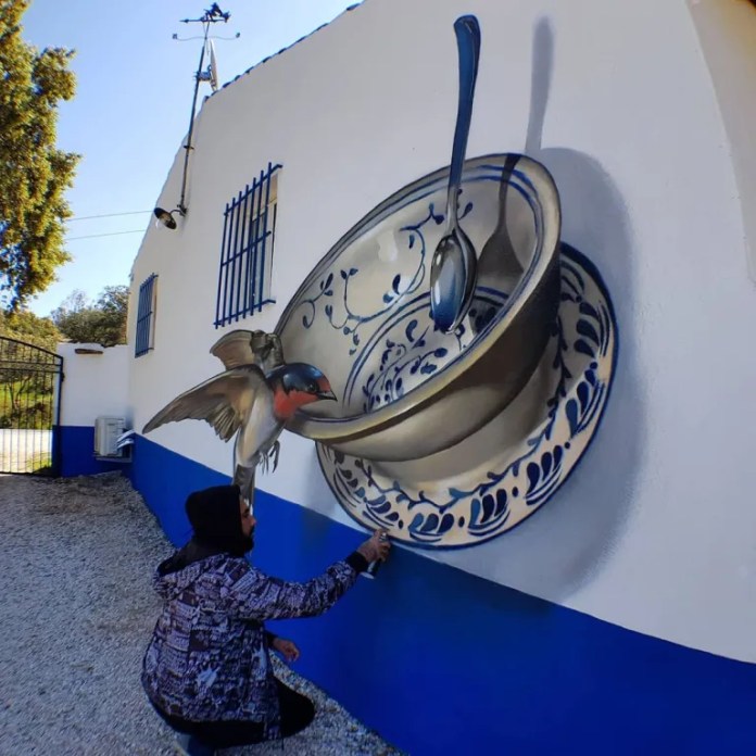 A hyperrealistic mural of a ceramic bowl and spoon painted on a wall in Portugal. A bird appears to perch at the edge, and the artist crouches beneath, seemingly touching the mural.