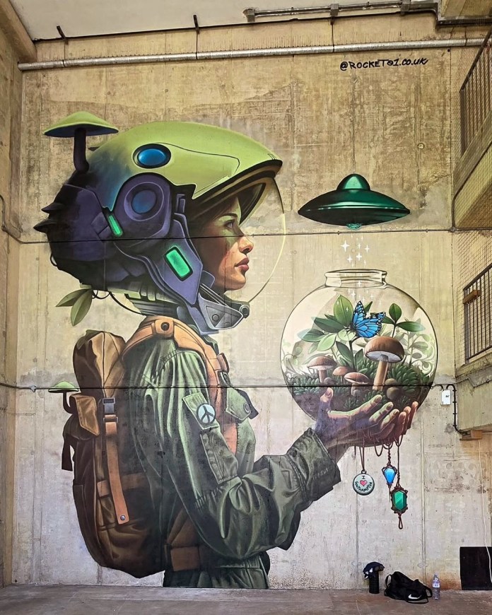 Mural of a woman in green space gear holding a glass terrarium with plants and mushrooms, a butterfly inside, and a UFO floating above. Painted on concrete in Southampton, UK by Chris Butcher.