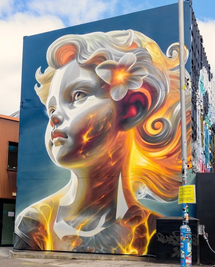 Hyper-realistic mural of a glowing child’s bust with fiery, lava-like textures beneath pale skin and swirling hair, featuring a white flower at the ear. Painted by Bacon in Glasgow, UK for Yardworks Festival 2025.