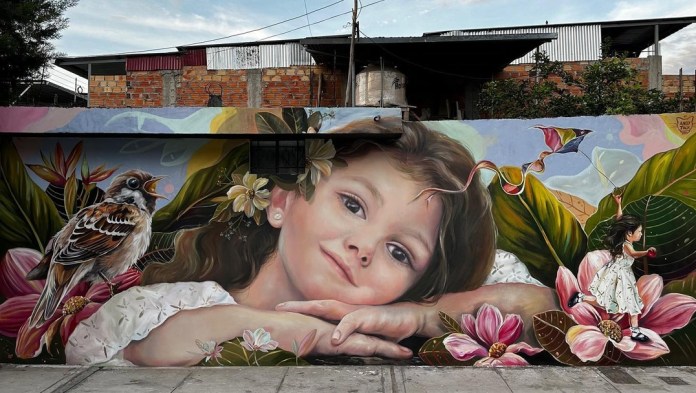 Mural of a girl lying with her head on folded arms surrounded by lush tropical flowers and birds, with a tiny version of herself flying a kite nearby in Moyobamba, Peru.
