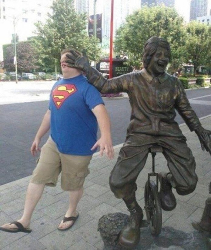 A bronze statue of a clown on a unicycle has its hand perfectly aligned over a man’s face as he walks by, making it appear as if the statue is slapping him.