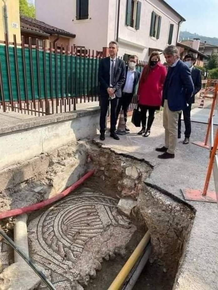 An ancient Roman mosaic with geometric patterns unearthed in Verona, Italy, buried beneath a modern street. Officials observe the excavation as the intricate tilework is exposed after centuries underground.