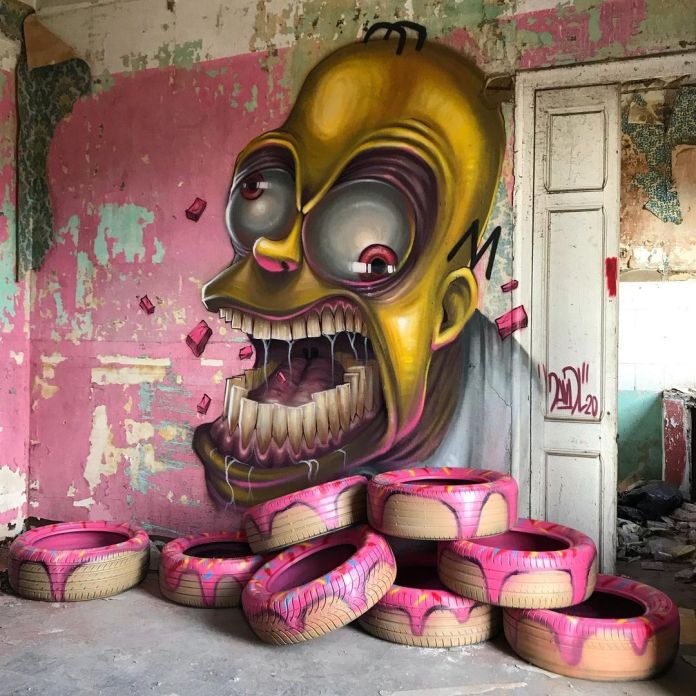 A twisted mural of Homer Simpson with exaggerated features and sharp teeth is painted inside an abandoned pink room, with painted tires shaped like donuts stacked below.