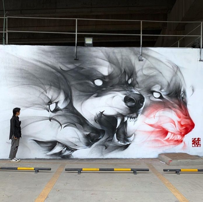 Monochrome street mural of three overlapping wolf heads, one highlighted with red tones, blending realistic features with a smoky abstract style. A person stands nearby for scale. Painted by Satr in Shanghai, China.