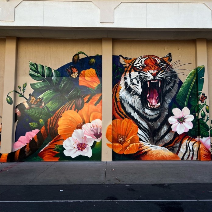 Colorful mural of a roaring tiger surrounded by large orange poppies, white flowers, and butterflies. Painted on a vertical panel façade in Modesto, CA.