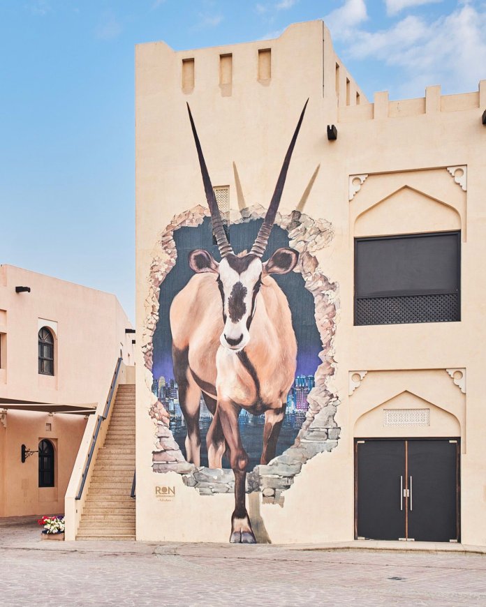 Large-scale mural of an oryx emerging through a broken wall with Doha’s skyline behind. Painted by Martín Ron in Qatar with strong photorealistic detail.