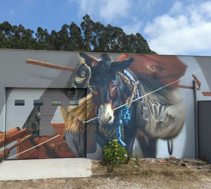 Detailed mural of a donkey carrying bundled supplies and ropes, painted on a building wall in Caldas da Rainha, Portugal. The donkey’s expression is calm and weary, and the scene includes realistic gear elements painted with depth and motion.