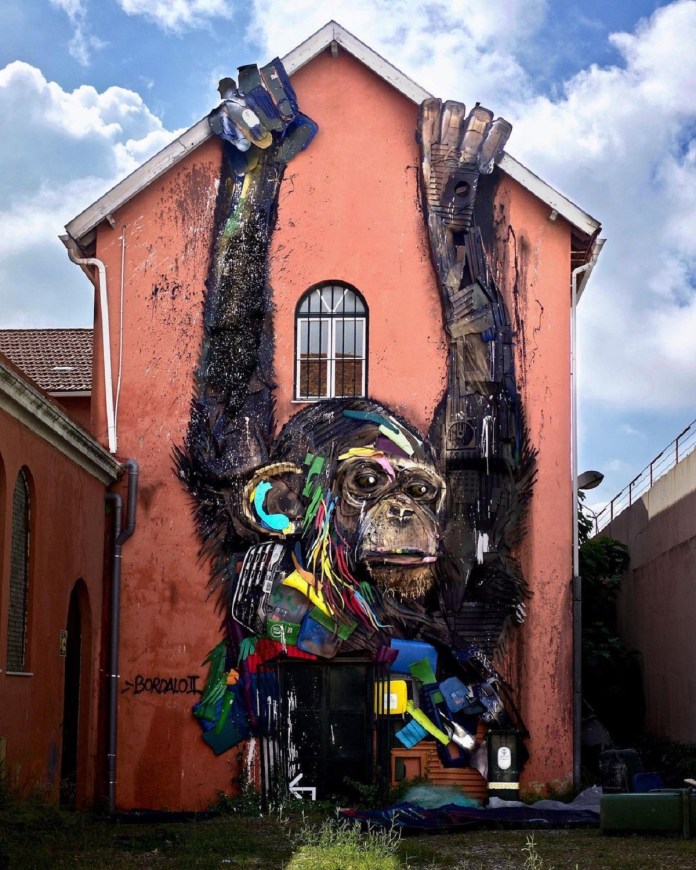Large chimpanzee mural made from recycled materials, extending from the wall of a peach-toned building in Lisbon. Created by BORDALO II.