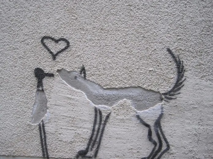 Wall art showing two dogs facing each other, with the peeling plaster forming one dog’s body and black outlines completing the legs and tails, with a heart above their heads.