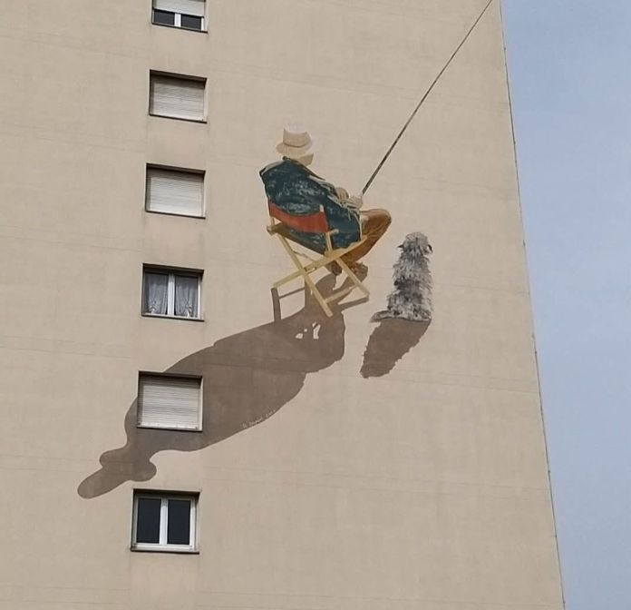 A mural by Louis Duport in Boissy-Saint-Léger, France, depicting a man fishing with a small dog beside him on a high-rise building, casting long shadows for a strong 3D effect.