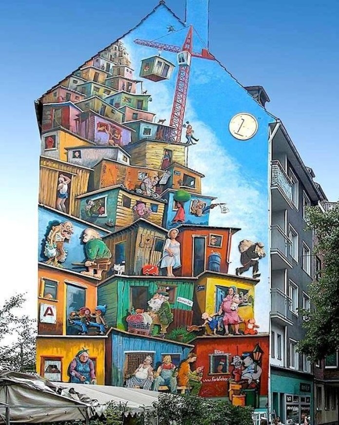 A colorful mural by Klaus Klinger in Düsseldorf, Germany, showing a stacked, chaotic cityscape with quirky characters, crooked houses, a crane, and social scenes painted on a tall building.