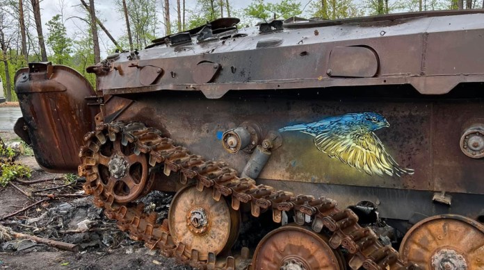 Street art by French artist Christian Guemy, known as C215, painted on the side of a destroyed and rusted military tank in Ukraine. The artwork features a small bird in vibrant blue and yellow hues, the colors of the Ukrainian flag, symbolizing hope, resilience, and the triumph of innocence over destruction. The tank's decayed and war-torn condition contrasts starkly with the peaceful and delicate image of the bird. This piece highlights the artist's commitment to creating poignant art in the midst of conflict, bringing messages of solidarity and peace to war-affected areas.