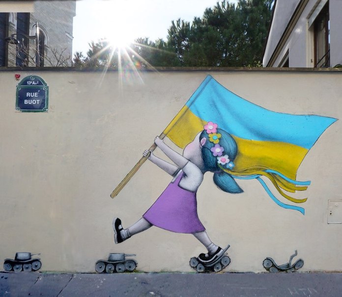 Mural by Paris-based street artist Julien Malland, known as Seth Globepainter, located in the 13th arrondissement of Paris. The artwork features a young girl in a purple dress with blue hair, wearing a floral headband, holding and waving a large Ukrainian flag in vibrant blue and yellow. She stands on small toy tanks transformed into roller skates, symbolizing resilience and the transformation of war into a message of hope. The bright sunlight in the background adds a sense of optimism, while the Rue Buot street sign provides the location. This piece blends themes of childhood innocence with the harsh realities of conflict, conveying a message of hope for a peaceful future.