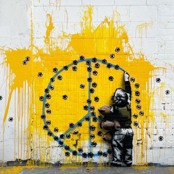 Mural by Los Angeles street artist HIJACK, featuring a poignant depiction of a child reaching up to paint a peace symbol on a wall. The peace symbol is rendered in blue against a backdrop of bright yellow, representing the Ukrainian flag, and is riddled with bullet holes, symbolizing the violence and destruction of war. The child, dressed in black and white, holds a teddy bear, emphasizing innocence amidst conflict. Yellow paint drips down the wall, reinforcing the raw, emotional tone of the piece. This artwork advocates for peace and highlights the plight of children affected by the war in Ukraine.