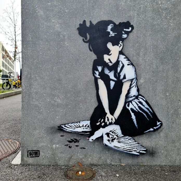 Stencil-style mural titled 'PɇaceMaker' located at the House of Peace in Geneva, Switzerland. The artwork depicts a young girl kneeling on the ground, her hands gently placed on a lifeless dove, a universal symbol of peace. The monochromatic design is contrasted by subtle shading, adding depth and emotion to the scene. The mural conveys a powerful and somber message about the fragility of peace and the impact of conflict. A nearby manhole cover and urban setting frame the artwork, reinforcing its integration into the city landscape as a poignant reminder of the need for harmony.