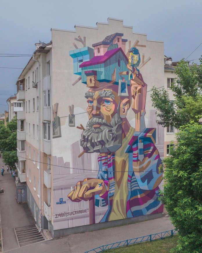 A mural by Iman in Ufa, Russia, depicting a bearded man in colorful, abstract shapes, with small house structures and birds incorporated into the head, suggesting memories or inner life.