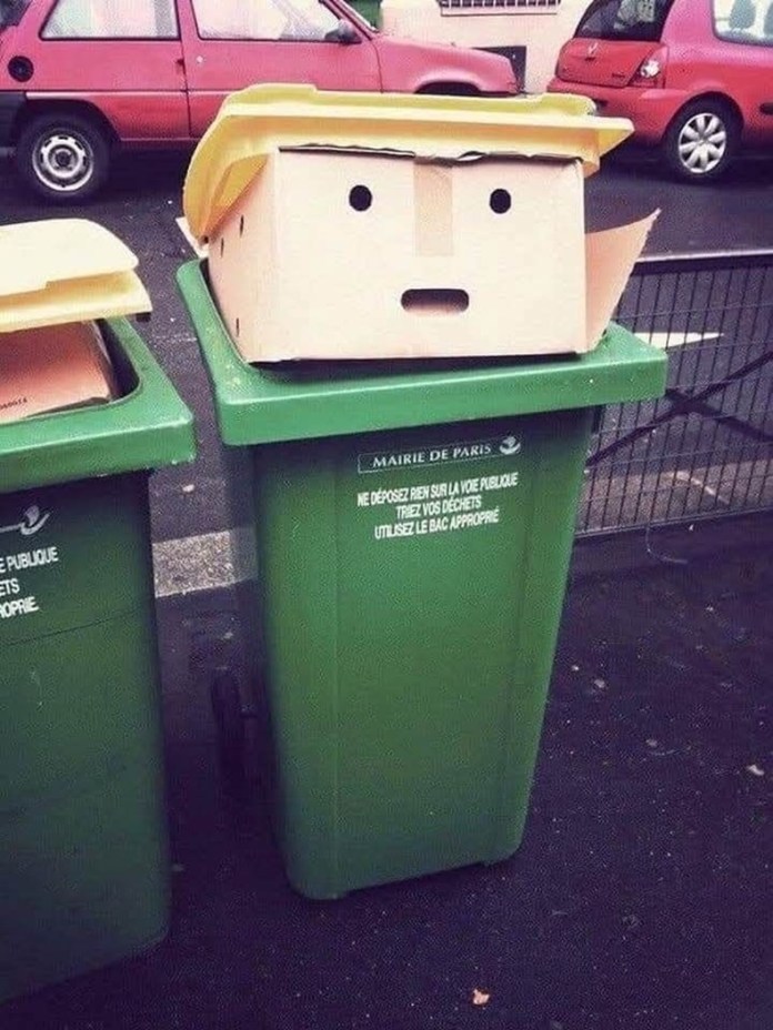 A green recycling bin in Paris with a box on top designed to look like a face with black-dot eyes and stylized yellow hair, resembling a parody of Donald Trump.