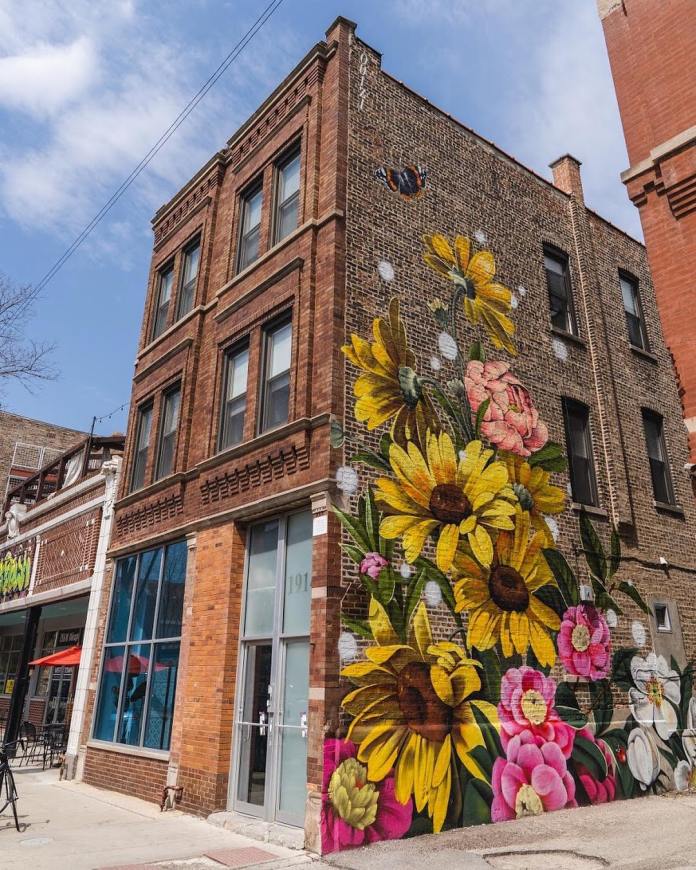 Floral mural featuring yellow daisies, pink peonies, white flowers, and a red admiral butterfly on the corner wall of a building in Chicago’s West Town by artist Ouizi (Louise Jones).