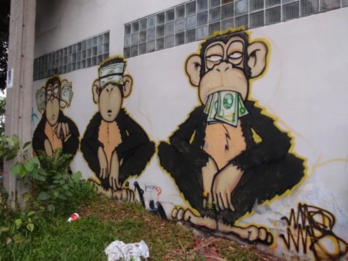 Mural of three chimpanzees on a white wall with dollar bills over their eyes, ears, and mouth respectively. The paint is bold, outlined in yellow, and surrounded by grass and trash.