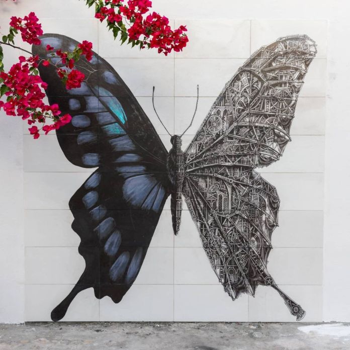 A black and white mechanical butterfly mural by Ardif in Erriadh, Tunisia, where one side of the butterfly is organic, while the other is made of intricate mechanical structures.