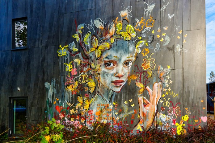 A mural by Herakut in Berlin, Germany, showing a melancholic female figure surrounded by expressive, sketch-like butterflies in muted tones.