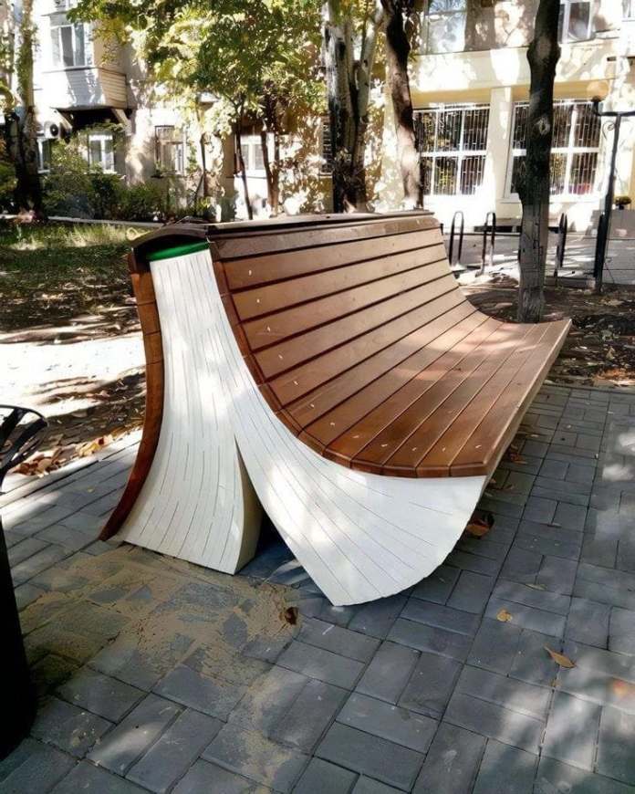 Curved wooden bench shaped like an open book, with brown slats forming the seat and white-painted sides resembling fanned pages, located near the city library of Zaporozhye, Ukraine.