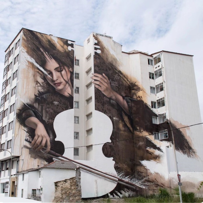 Large mural of a woman playing a violin, her body aligned with the structure of a high-rise building in Fene, Spain.