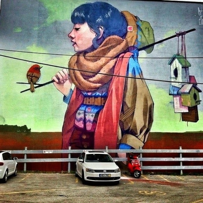 Large mural of a girl with a scarf and bundled clothing holding a stick with birdhouses and a bird perched on it, painted on a wall in Montreal.