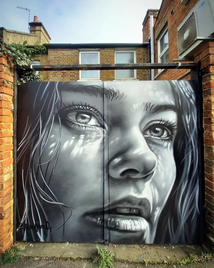 Black-and-white mural of a woman’s face painted on metal doors in London, with detailed eyes, glistening lips, and strands of wet hair.