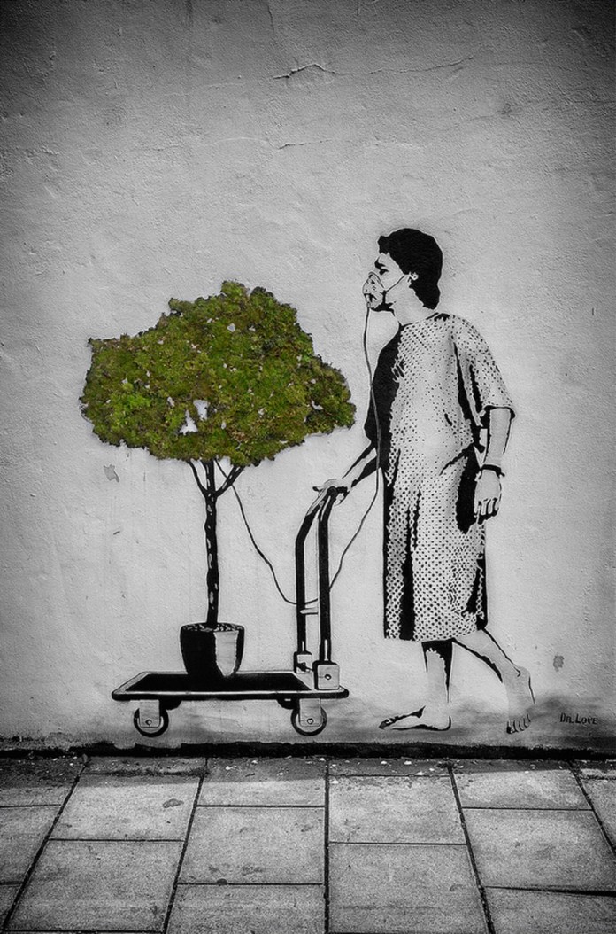 Mural of a barefoot patient pulling a cart with a real moss-covered tree while using it as an oxygen source, painted by Dr. Love in Bristol.