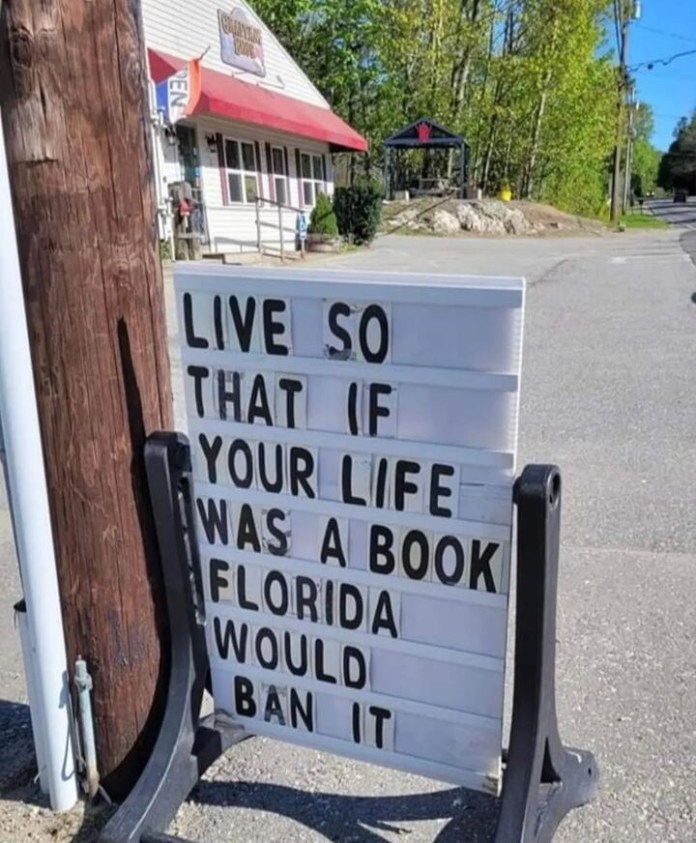 Plastic board outside a shop with black letters spelling out “LIVE SO THAT IF YOUR LIFE WAS A BOOK FLORIDA WOULD BAN IT,” addressing censorship and personal freedom.