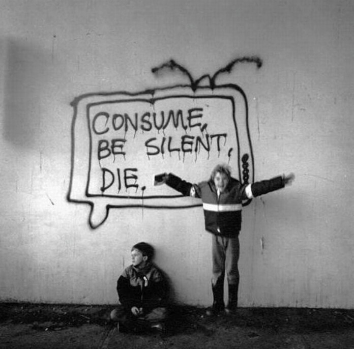 Black-and-white image of two children in front of a graffiti TV frame with the text “Consume, be silent, die” dripping in spray paint.