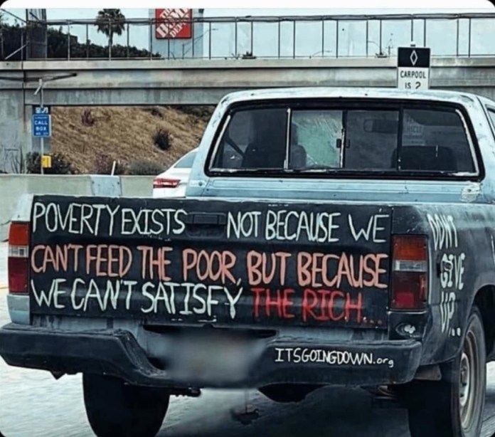 Back of a gray pickup truck with message: “Poverty exists not because we can’t feed the poor, but because we can’t satisfy the rich,” painted in black and red letters.
